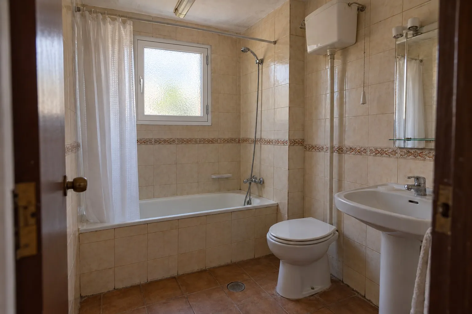 Baño con bañera, cortina y azulejo con cenefa en un piso de El Calvario, Torremolinos, antes de la reforma